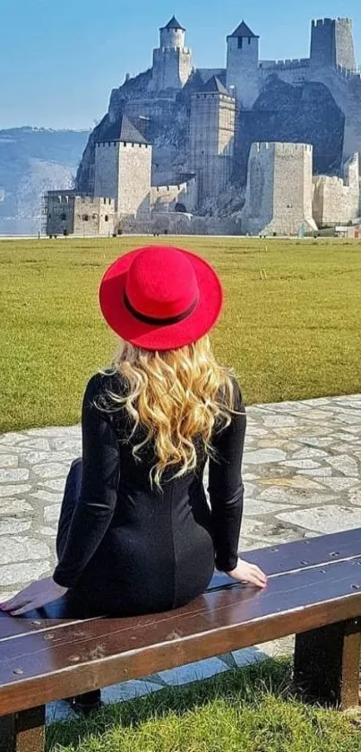 Woman in red hat sits facing a castle with scenic view.