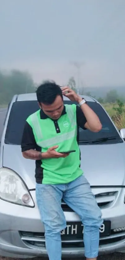 Person in green shirt leaning against a silver car.