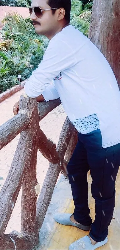 Man with sunglasses leaning on balcony surrounded by nature.