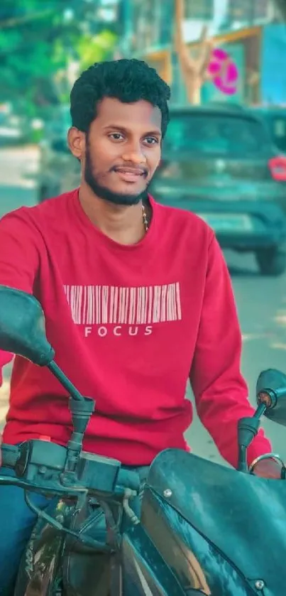 Man in red sweater on black motorcycle outdoors.