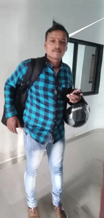 Man wearing blue plaid shirt holding helmet indoors.