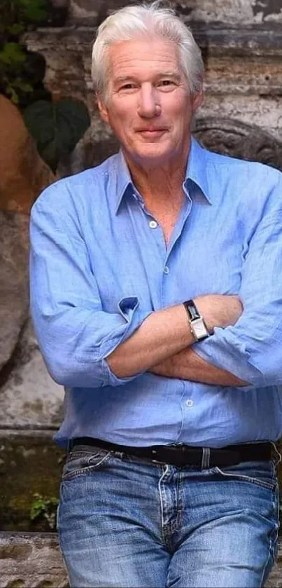 Man in blue shirt standing against stone wall outdoors.