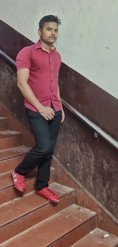 Man in red shirt leaning on a staircase, casual fashion vibe.