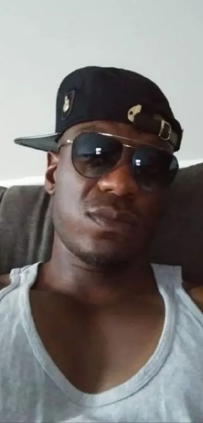 Person wearing sunglasses and cap against gray background.