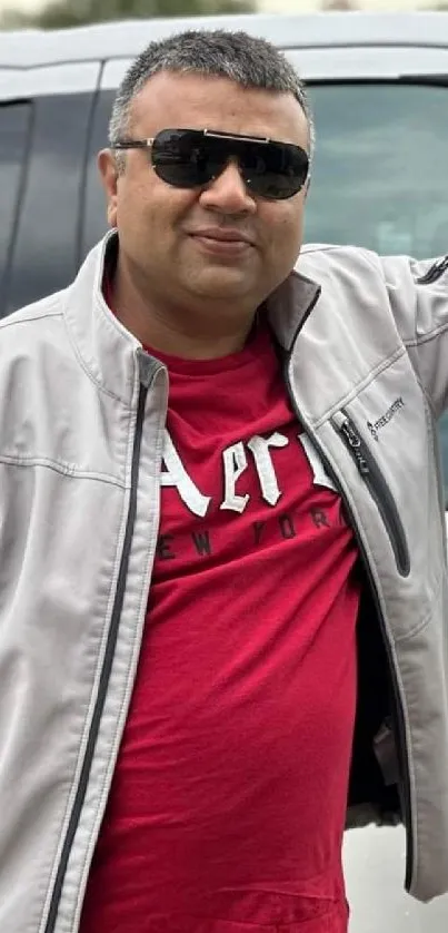 Man in sunglasses wearing a gray jacket and red shirt.