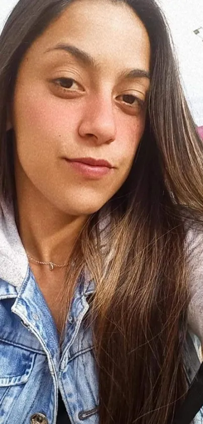 Young woman in denim jacket posing outdoors with a natural background.