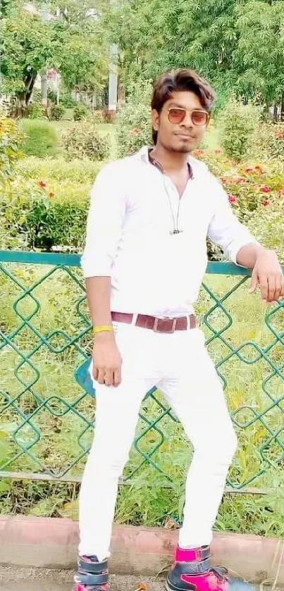 Man in white outfit leaning on a fence in a lush green garden.