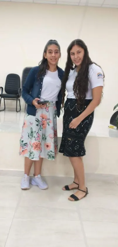 Two women in floral skirts pose stylishly indoors.