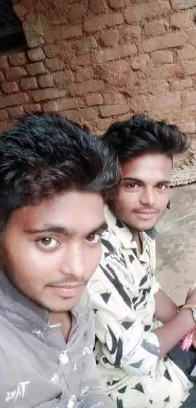 Two friends smiling in front of a brick wall.