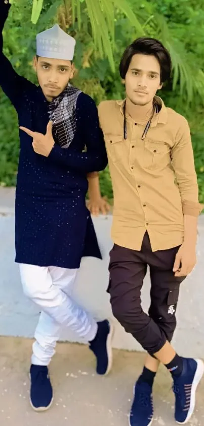 Two friends in casual attire posing outdoors with a green background.