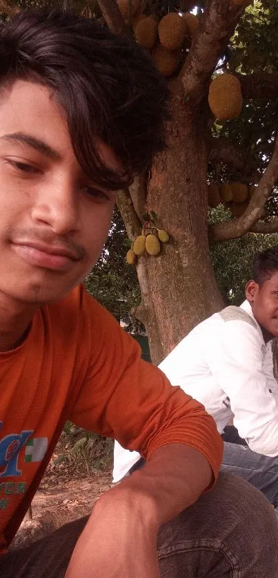 Two friends relaxing under a fruit tree outside.