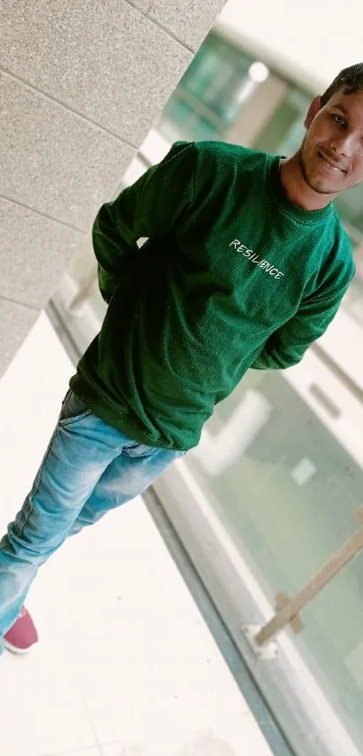 Man in green sweater and jeans standing indoors.