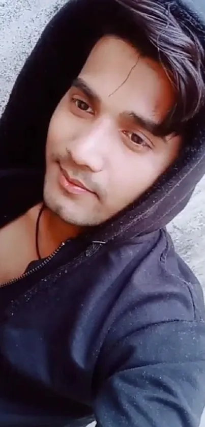 Person in a black hoodie against a textured wall.