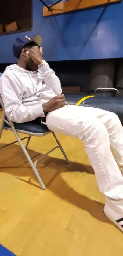 Person in casual wear sitting indoors on a chair in a gym setting.