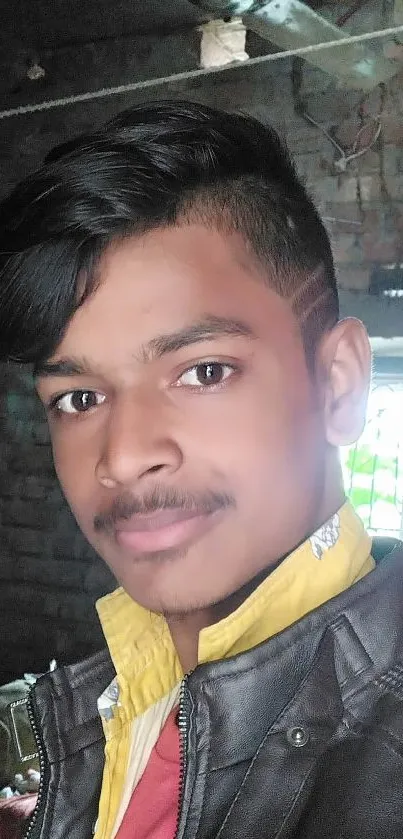 Young man in black jacket indoors with brick wall background.