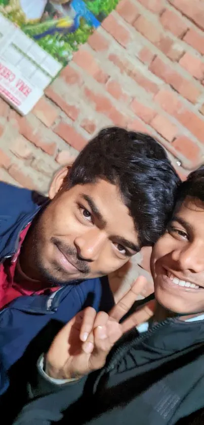 Two friends taking a selfie indoors against a brick wall.