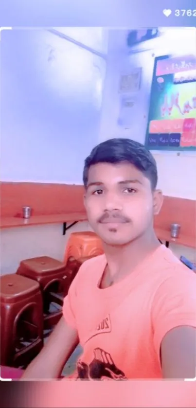 Selfie of a young man indoors wearing an orange shirt.