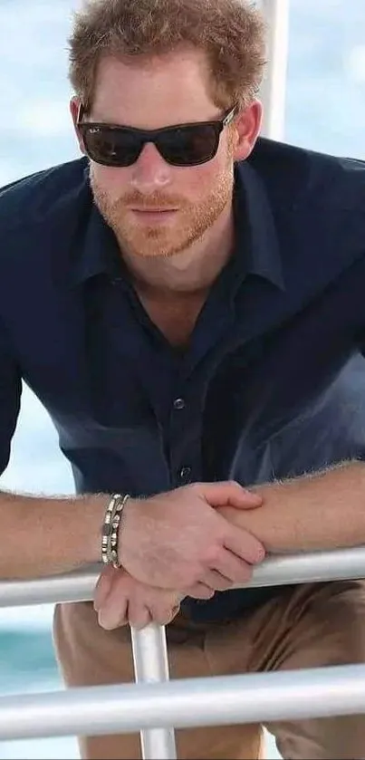 Man in sunglasses leaning on a railing with ocean backdrop.