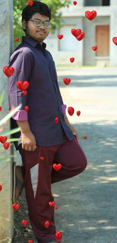 Young man posing outdoors in casual attire, leaning against a wall.