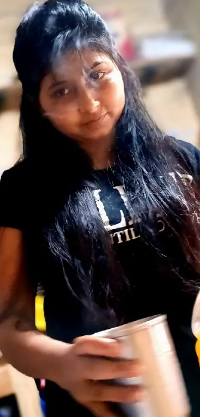 Young woman in black t-shirt holding a cup at home.