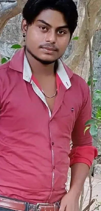 Man in red shirt posing outdoors with trees and nature background.