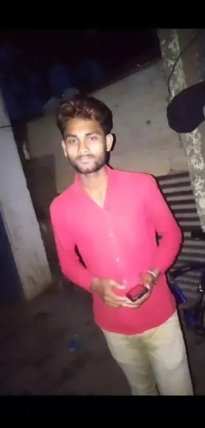 Man in red shirt poses in urban street at night.