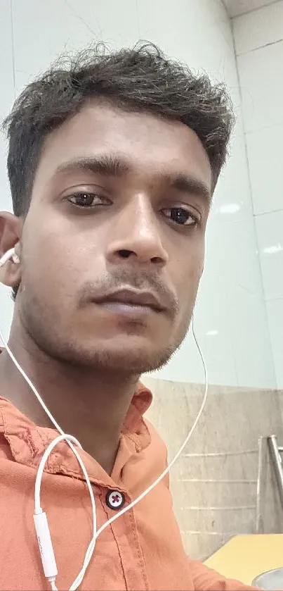 Portrait of a young man in an orange shirt with earphones.