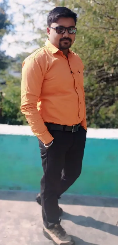 Man in orange shirt standing outdoors on a sunny day.