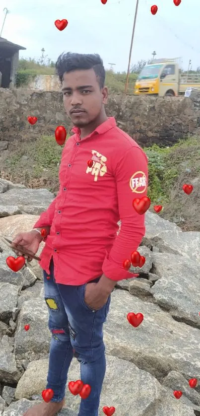 Man in a red shirt on rocky terrain with a cloudy sky.