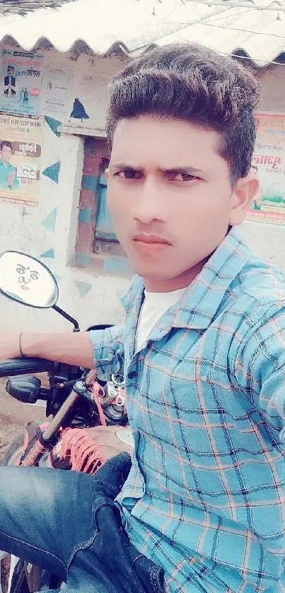 Young man in blue plaid shirt taking a selfie on a bike outdoors.