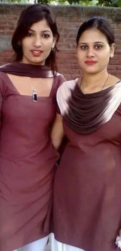 Two women in brown outfits posing outdoors.