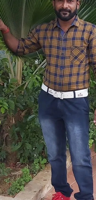 Man in plaid shirt with jeans standing outdoors.