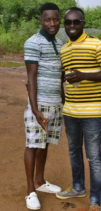 Two friends smiling outdoors in striped shirts.