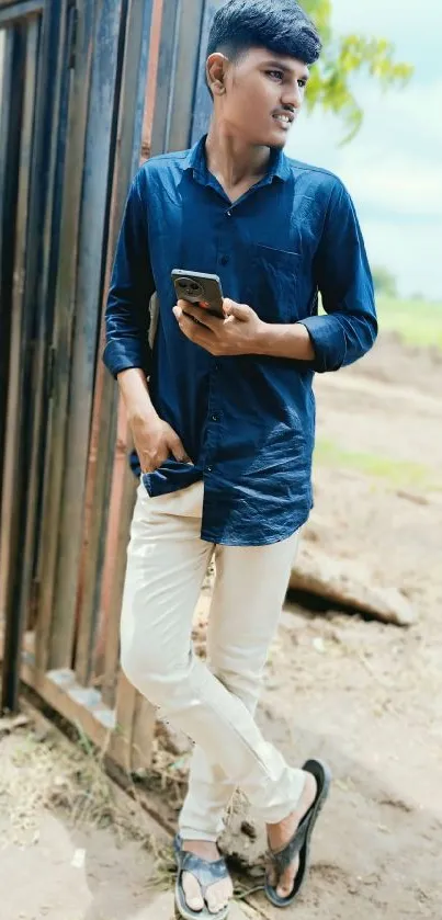 Young man in blue shirt holding a phone outdoors.