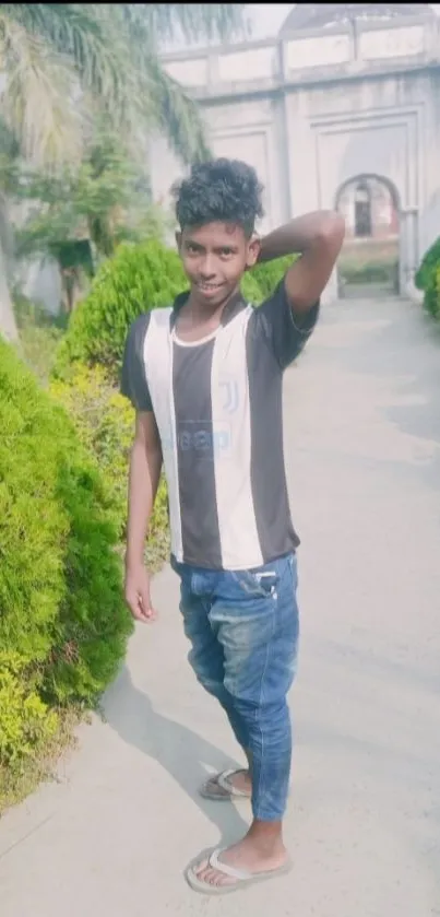 Young man posing on a garden pathway with greenery.