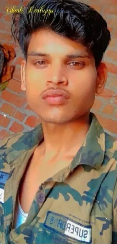 Young man in camo with brick wall backdrop.