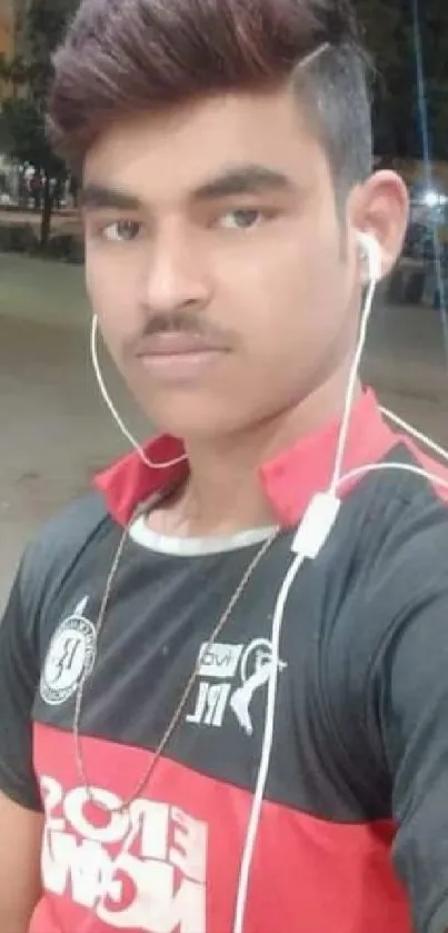 Young man in dark red shirt and headphones in outdoor setting.