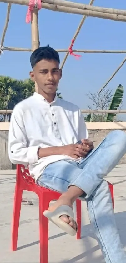 Young man sitting casually outdoors on a red chair.