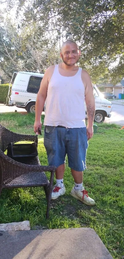 A man in casual attire outdoors with greenery and natural light in a suburban setting.