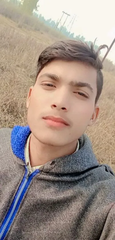 Young man in hoodie outdoors with rustic background.