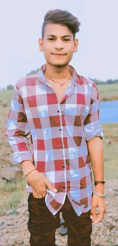 Young man in a red plaid shirt standing outdoors with a natural background.