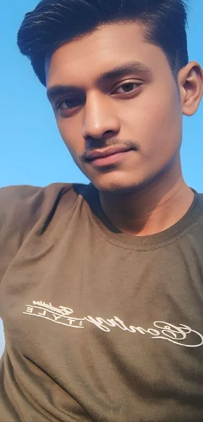 Young man posing outdoors with blue sky background.