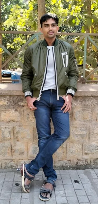 A man poses casually outdoors with a green jacket and jeans.