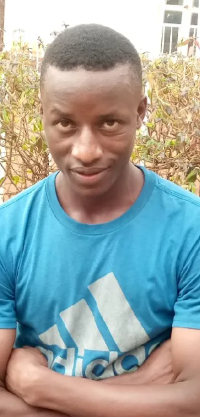 Outdoor portrait of a man in a blue shirt, arms crossed, with a natural background.