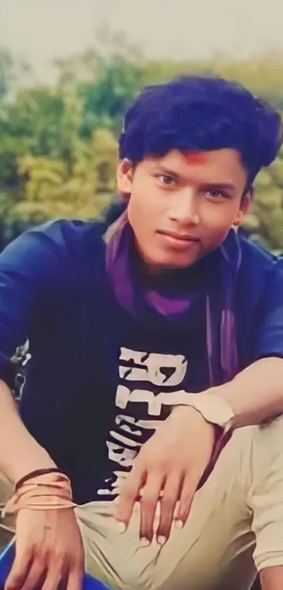 Young man casually seated outdoors with a green nature background.