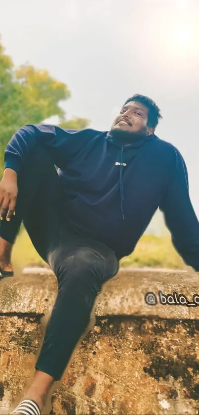 Casual man in blue hoodie sitting outdoors.