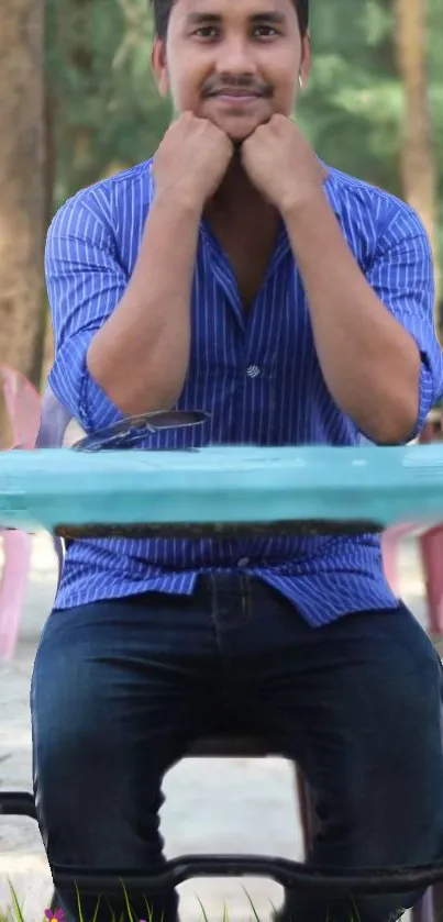 Man in blue shirt sits outdoors at a table.