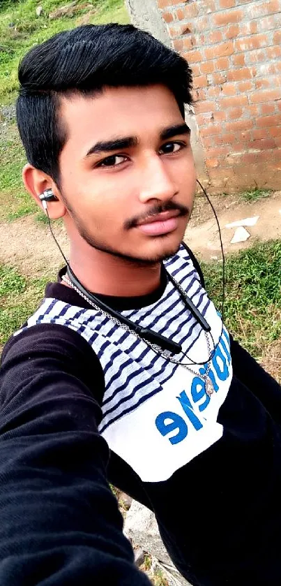 Young man takes a selfie outdoors in a casual striped shirt with a natural background.