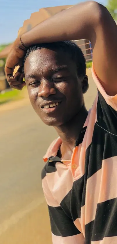 Young man smiling outside in sunlight, casual fashion.