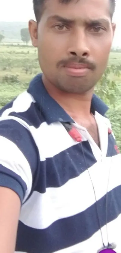 Casual selfie in striped shirt with nature background.